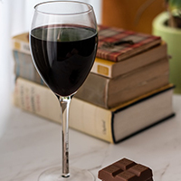 Photo of a glass of wine next to some chocolate in front of some books