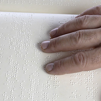 Photo of someones hand on a sheet of Braille
