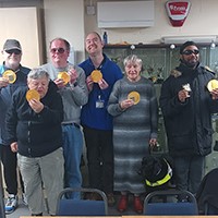 Photo of a group of people holding medals and smiling at the camera at the shooting club