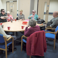 Photo of people sat around a table in the support group with a cuppa