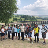 Photo of the walking group standing in a row in front of a lake with a bridge in the background