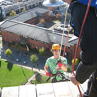 Photo taken from above of someone abseiling down the side of  the Owen Building in Sheffield. The view looks down on some smaller buildings 